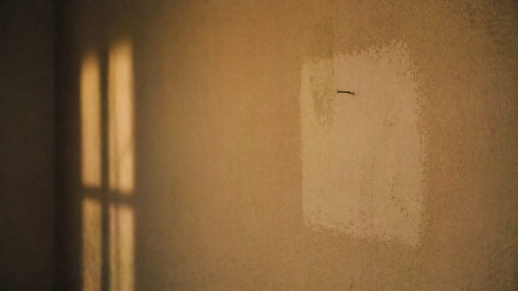 フリーランス医師3年目でも消えない漠然とした不安を象徴する、額縁を外した跡だけが残る壁と小さな釘、差し込む斜めの光
